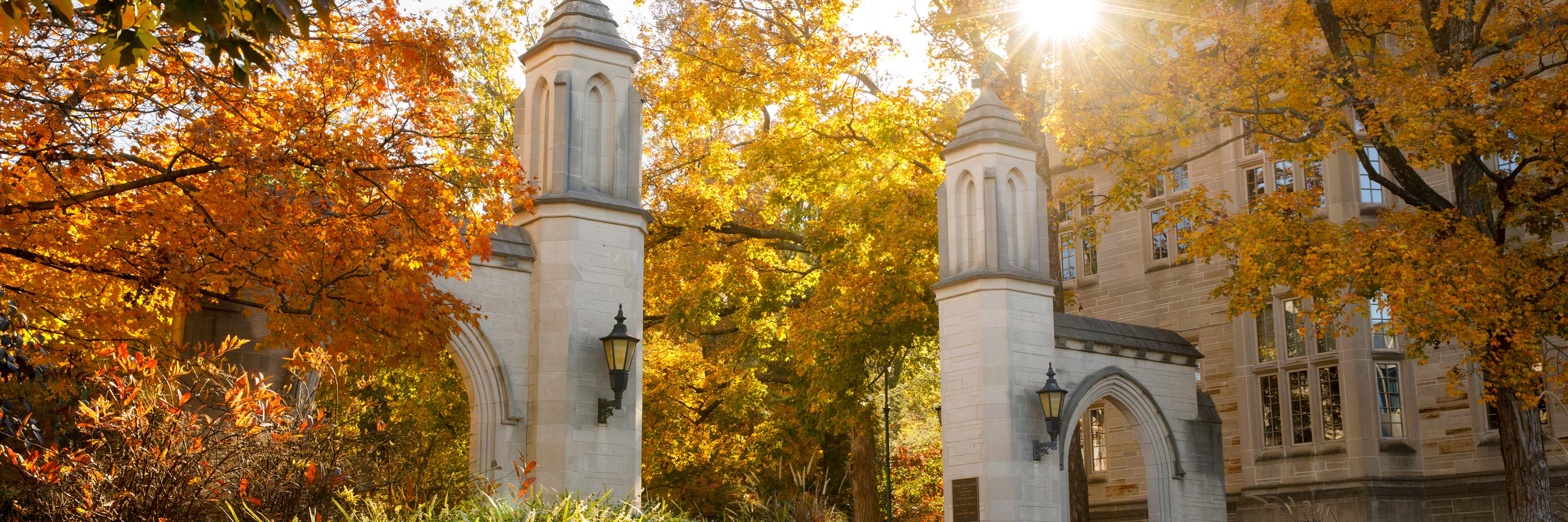 Photo of iconic Sample Gates of IU campus with the sun filtering through colorful fall leaves.