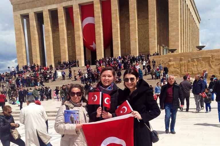 Three students pose holding small flags of Turkey, the country in which they're studying abroad