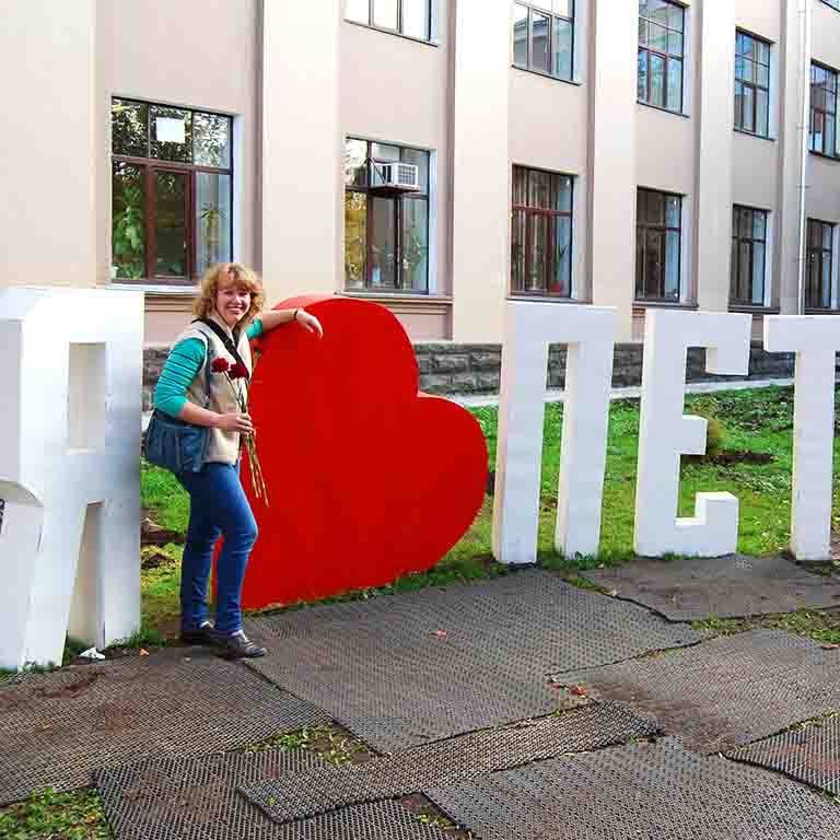 A student stands near a sculpture with Russian words.