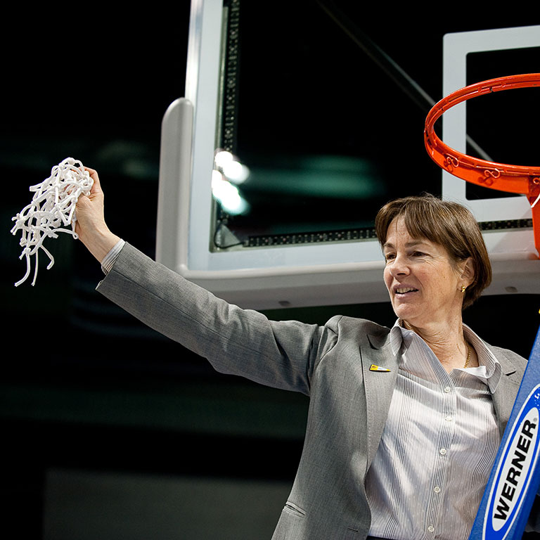 Tara VanDerveer holds up the net of a basketball net