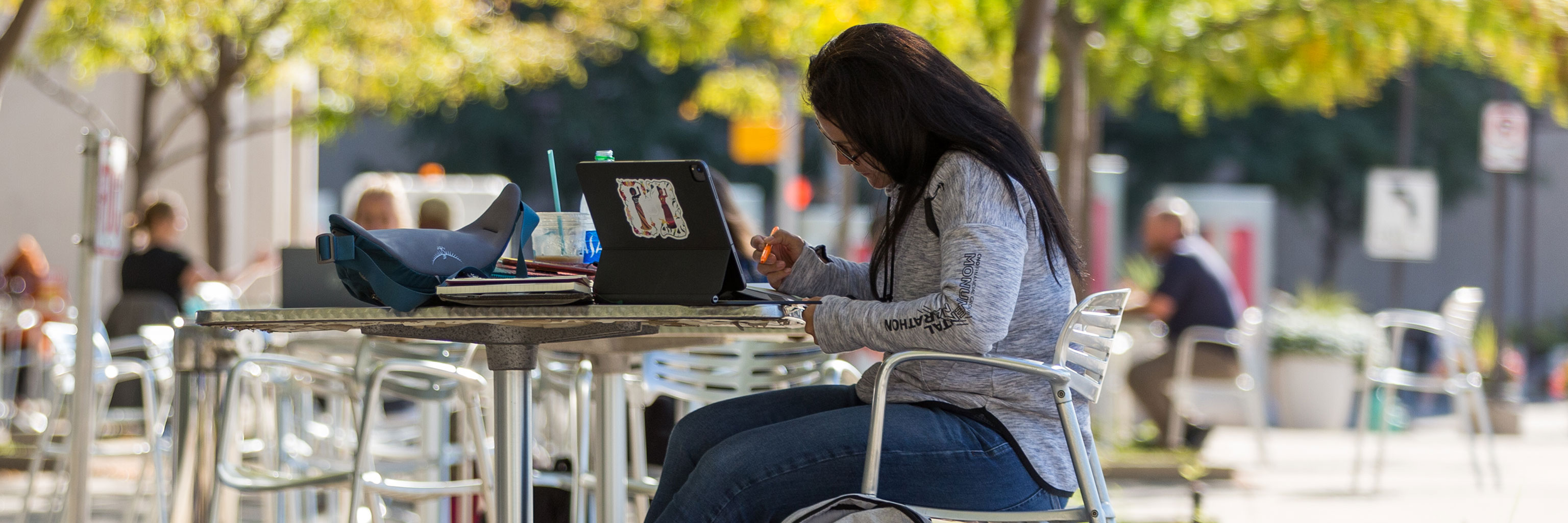 A student sits in front of a laptop outdoors, taking notes.