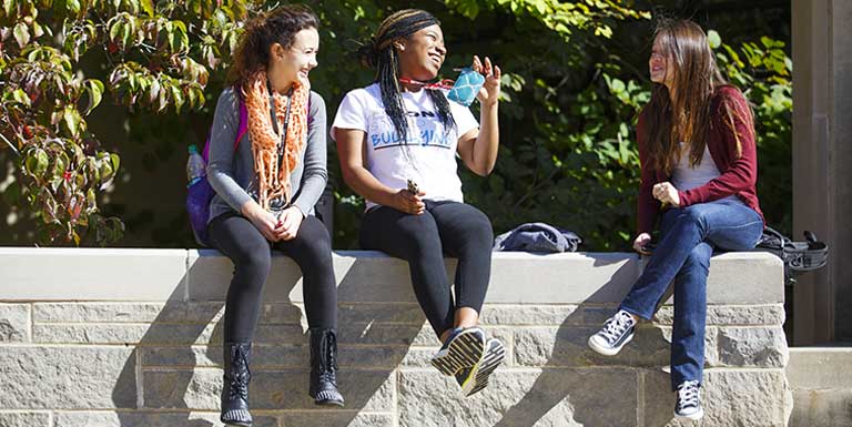 Three students laughing and sitting on a wall