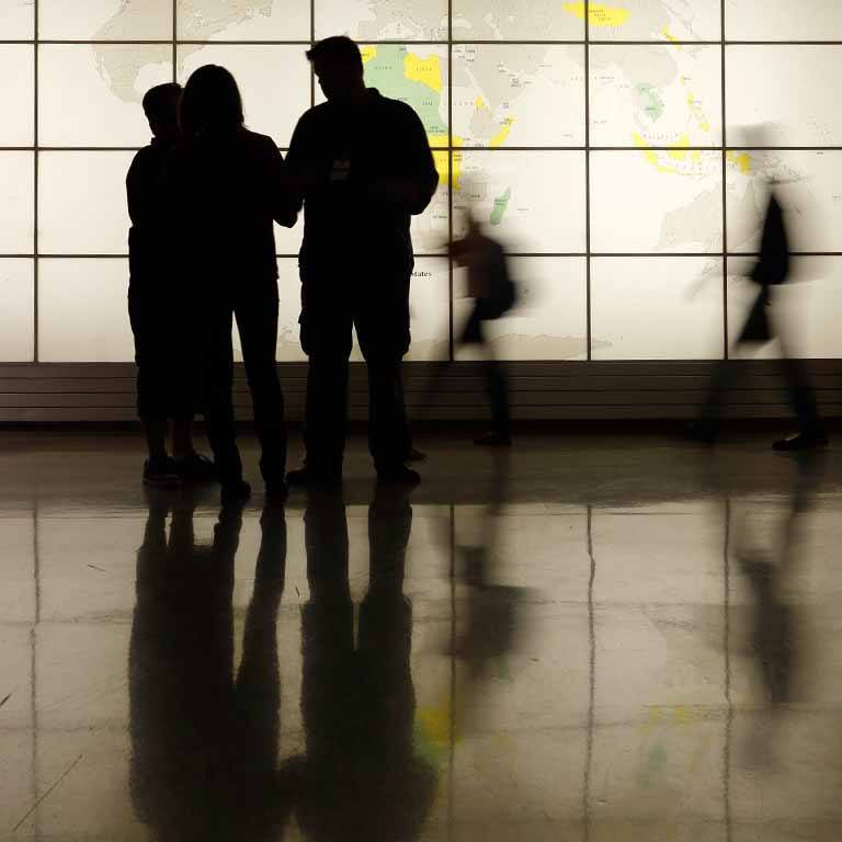 Silhouetted people stand in front of a world map.