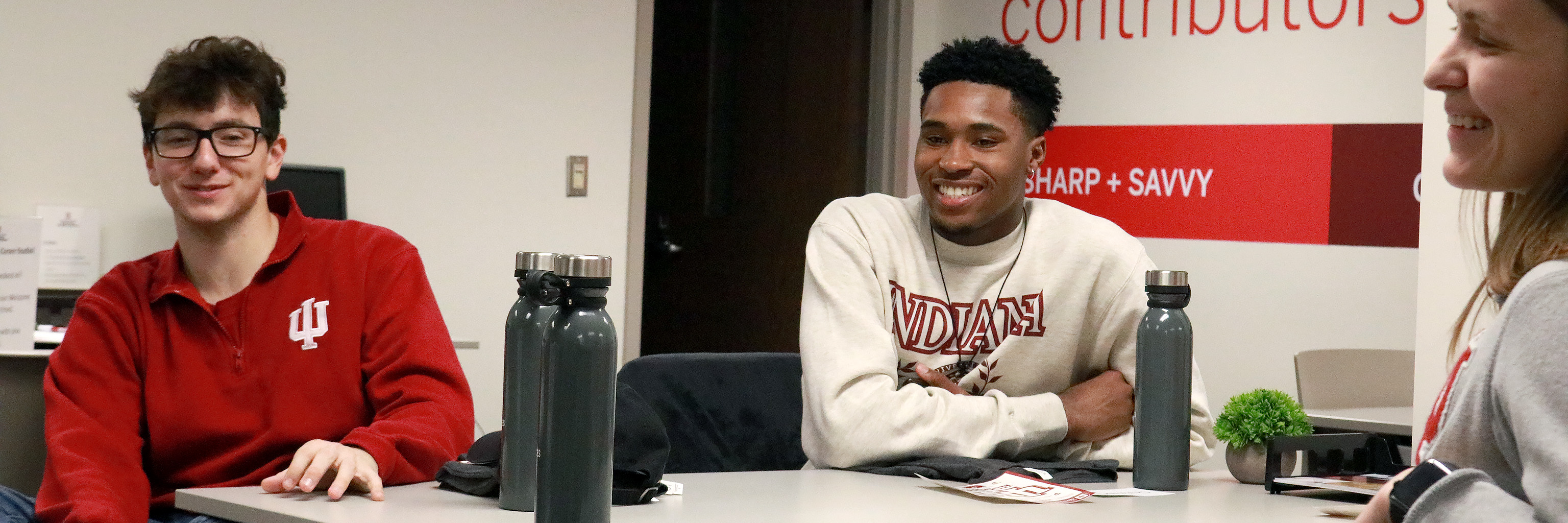 Three students wearing IU attire sit at a desk, smiling