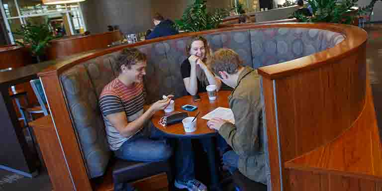 Laughing students gather around a table in a dining hall.